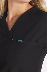 Woman wearing black drop shoulder black scrub top with two pockets and dolan logo