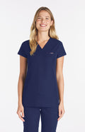 Woman wearing navy Nava drop shoulder black scrub top with two pockets and dolan logo
