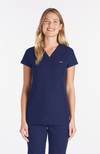 Woman wearing navy Nava drop shoulder black scrub top with two pockets and dolan logo