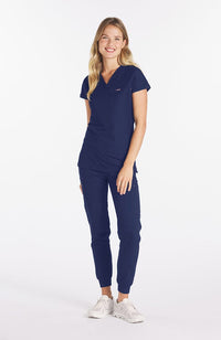 Woman wearing navy Nava drop shoulder black scrub top with two pockets and dolan logo