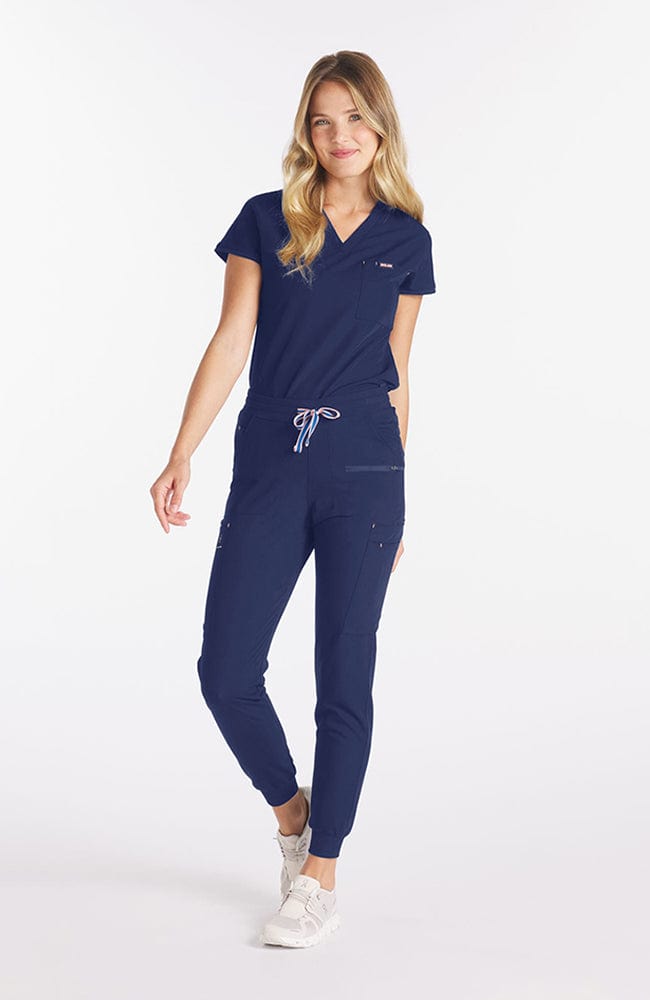 Woman wearing navy Nava drop shoulder black scrub top with two pockets and dolan logo