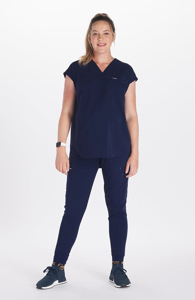 A pregnant woman wearing the DOLAN Pia Maternity Scrub Top 2-Pocket CORE and SOFIA Maternity Jogger Scrub 8-Pocket CORE in Navy while putting her hand on her stomach. 