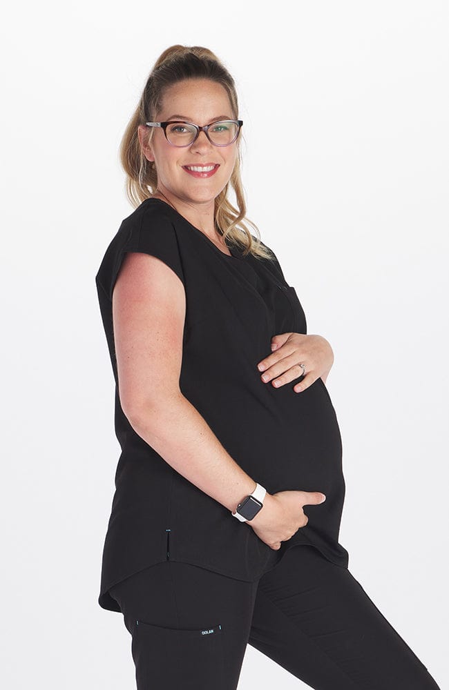 A pregnant woman wearing the DOLAN Pia Maternity Scrub Top 2-Pocket CORE and SOFIA Maternity Jogger Scrub 8-Pocket CORE in Black while putting her hand on her stomach. 